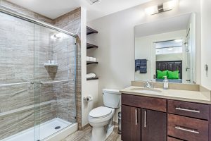 A modern bathroom with sliding glass door shower, toilet, and sink with cabinets