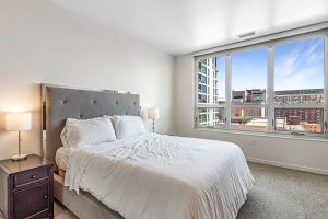 A bedroom with a large bed and night stands with lamps on either side on an upper level of an apartment building