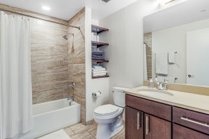 A modern bathroom with bathtub, built in towel shelves, toilet, and sink with cabinets