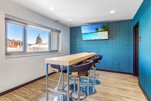 A high table with bar stools around it with a TV on the wall and a view of the Madison, WI capitol building out the window