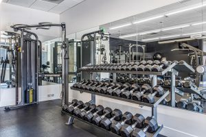 A gym with a mirrored wall and racks of free weights