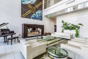 A common area in an apartment building with couches, a baby grand piano, and a gas fireplace