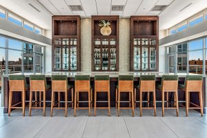 A beautiful bar area with stools and large wood and glass cabinets holding various drinking glasses and plates