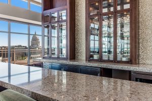 A beautiful bar area with large wood and glass cabinets holding various drinking glasses and plates, and a view of the Madison, WI capitol building