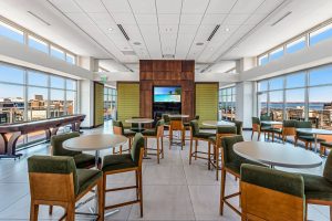 A common room in an apartment building in a tall building with a shuffle board, tables and chairs, a wall-mounted TV and a gas fireplace